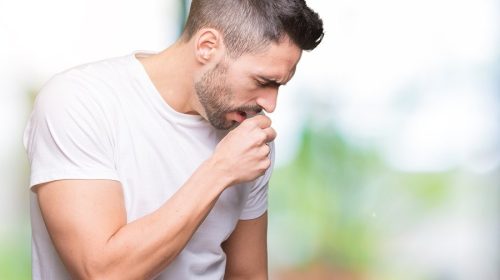 Young man wearing casual white t-shirt over isolated background feeling unwell and coughing as symptom for cold or bronchitis. Healthcare concept.